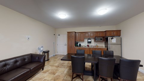 A brown leather couch sits in a living room with a kitchen in the background.