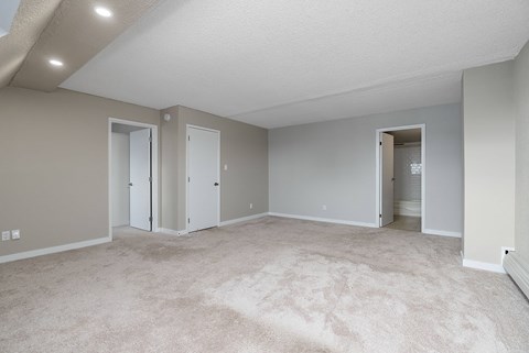 A spacious room with carpeted floor and three doors.