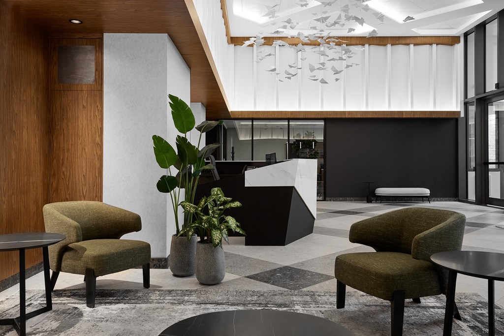 A modern office space with a reception desk, chairs, and a potted plant.