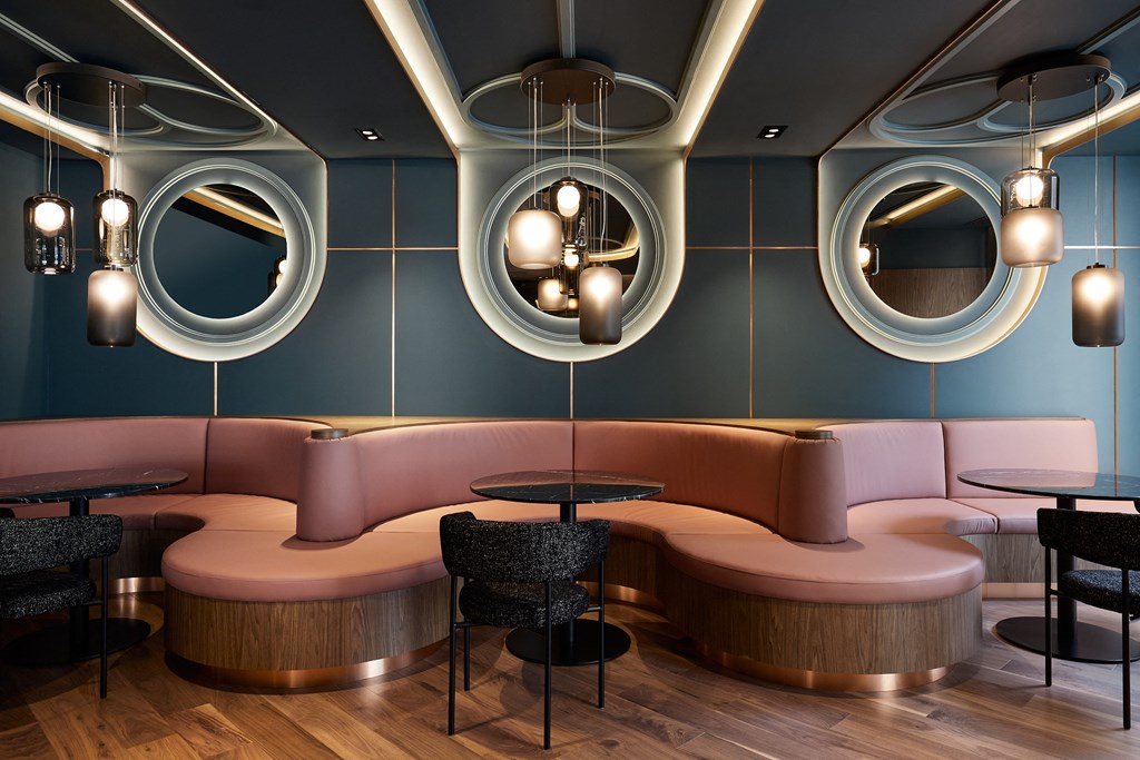 A modern restaurant with a curved pink sofa and round mirrors on the wall.