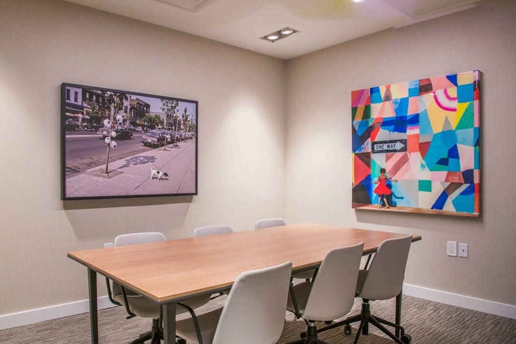 A conference room with a large table and chairs and two pieces of artwork on the wall.