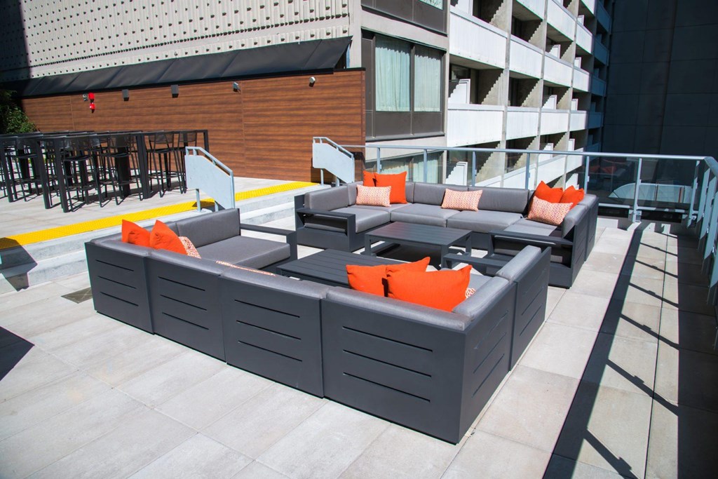 A grey couch with orange pillows is on a patio.