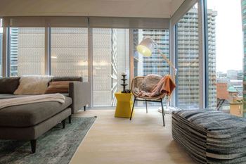 A modern living room with a grey sofa, a yellow side table, and a large window overlooking a cityscape.