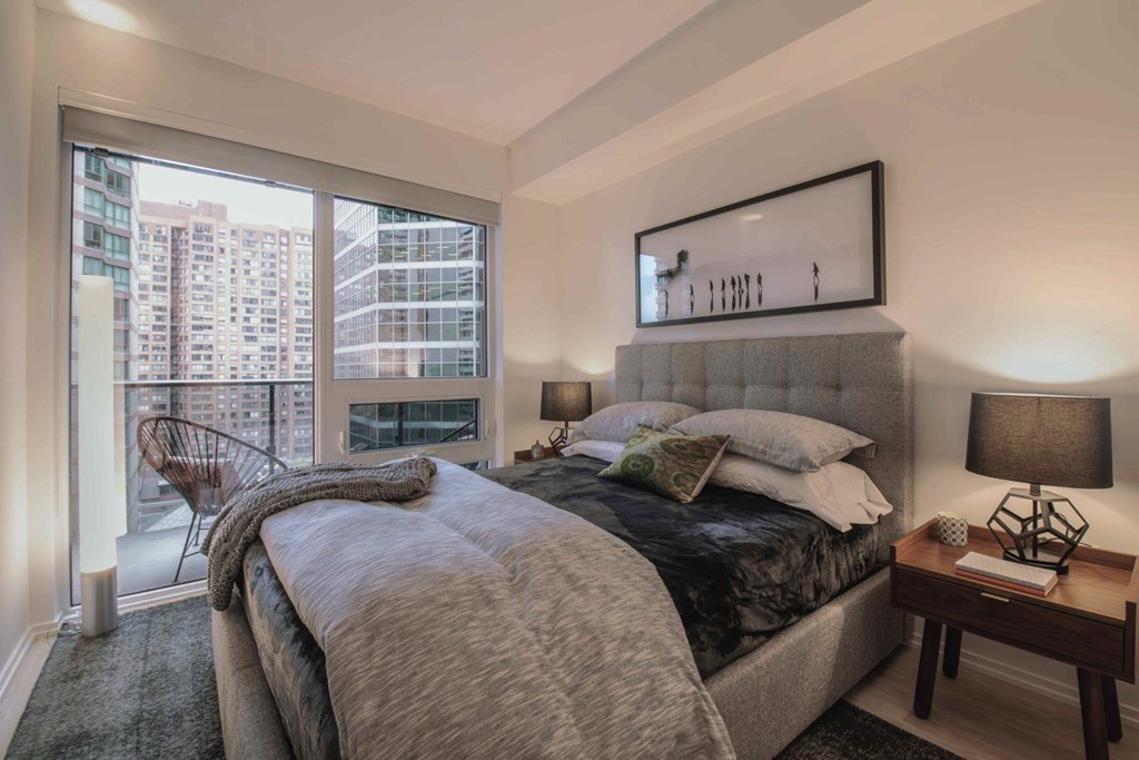 A bedroom with a large bed and a city view through the window.