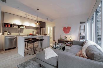 A modern living room with a grey couch and a kitchen area in the background.