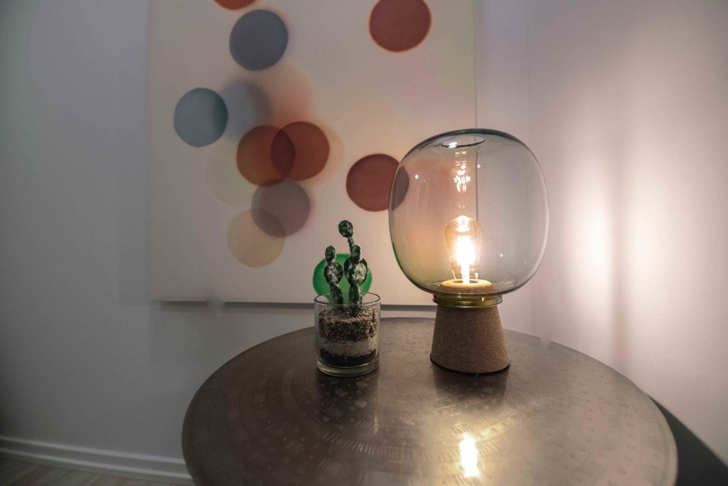 A small cactus sits on a table next to a light bulb in a glass dome.