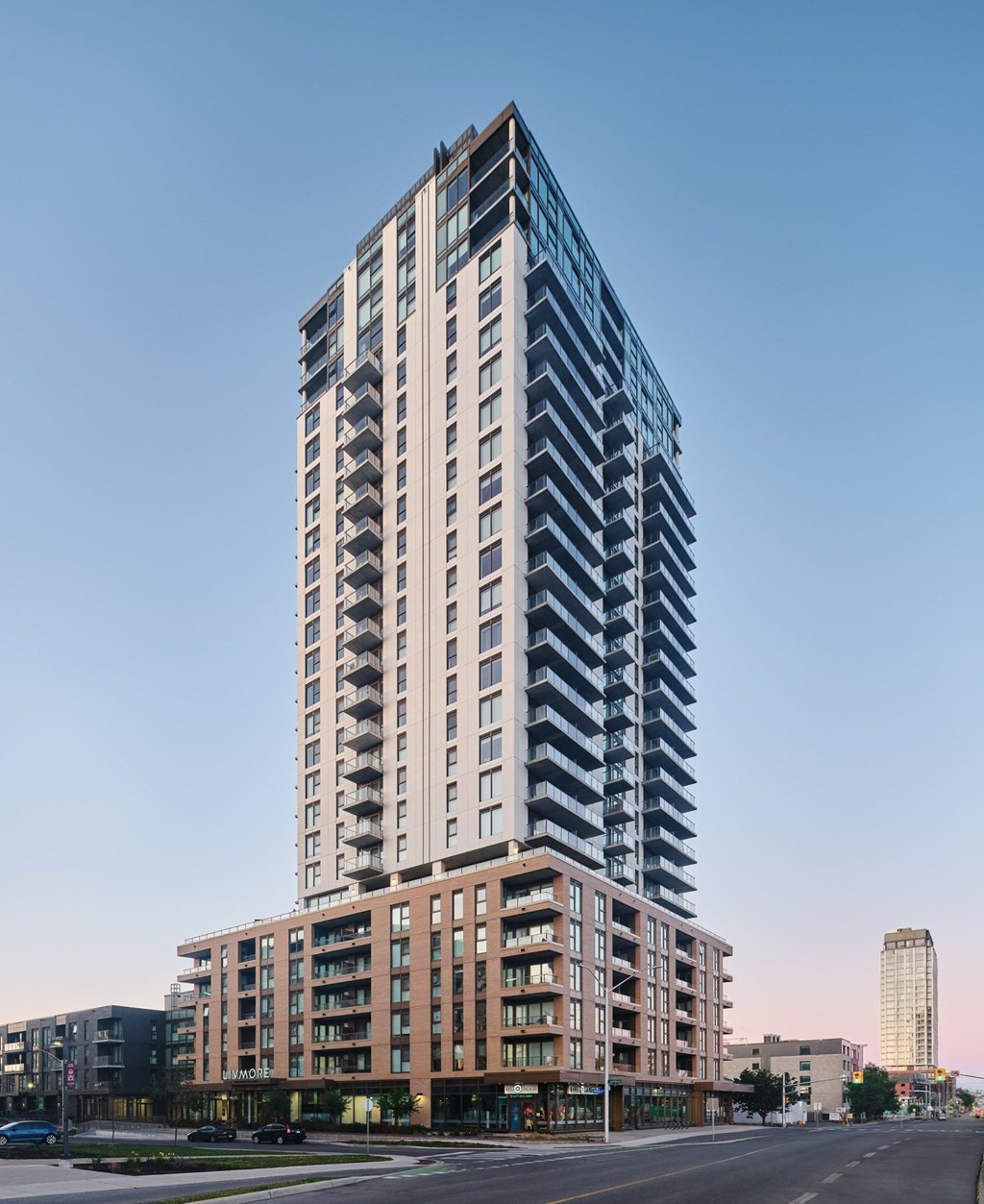 A tall building with a glass facade stands in the foreground of a city street.