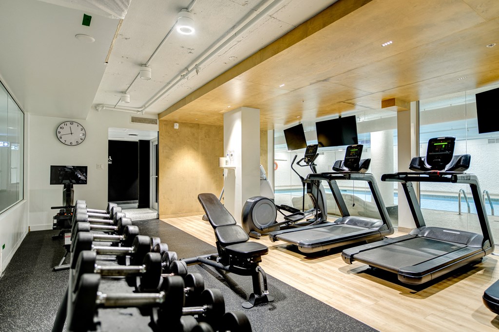 a gym with treadmills and weights and a clock on the wall