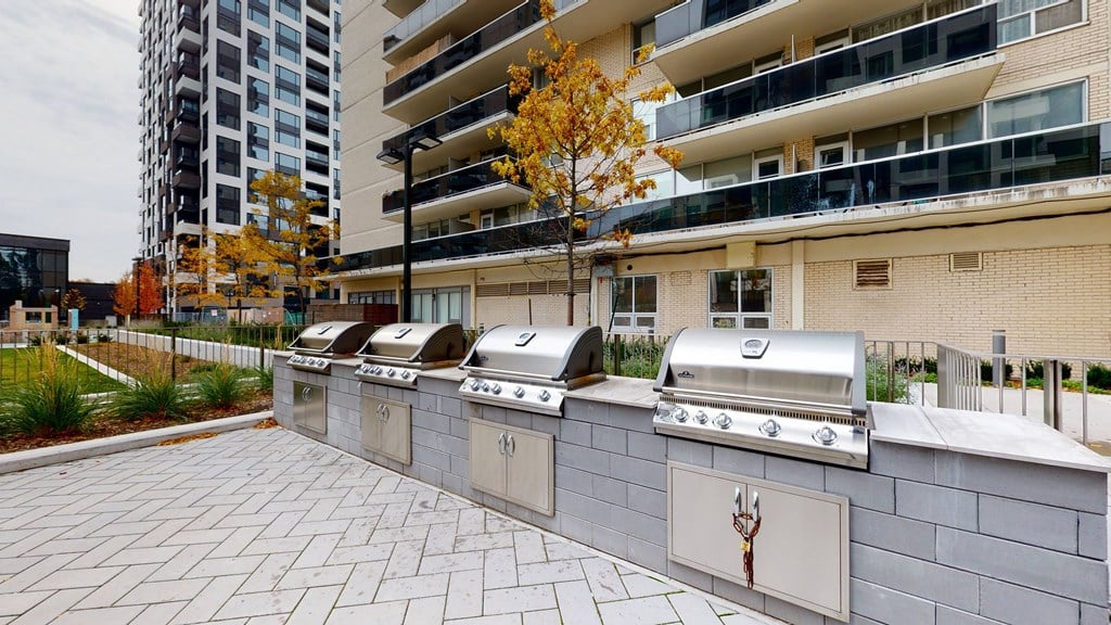 A row of outdoor grills are lined up on a brick patio.