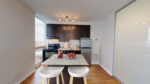A kitchen with a table and chairs in the foreground and a refrigerator, microwave, and oven in the background.