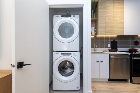 A white front loading washing machine is in a cabinet in a kitchen.