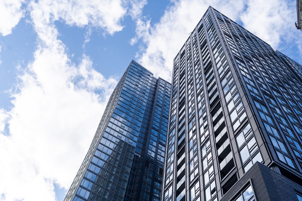 Two tall buildings with glass windows and a blue sky with clouds in the background.