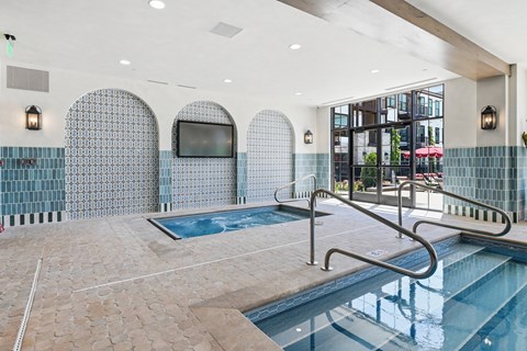 A swimming pool inside a building with a television on the wall.