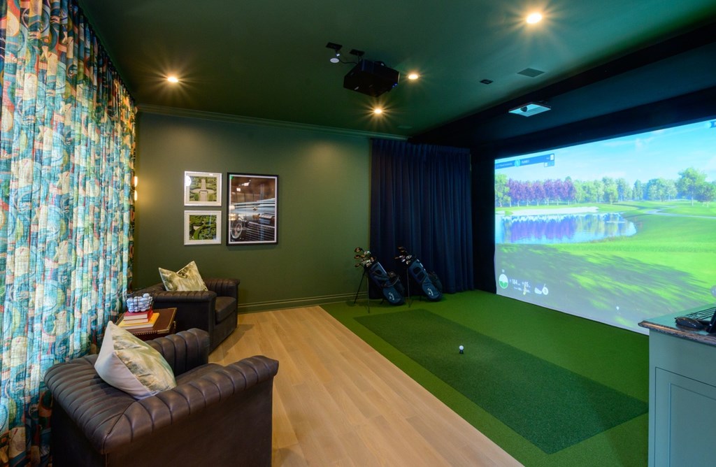 A room with a couch, a screen, and a golf simulation setup.