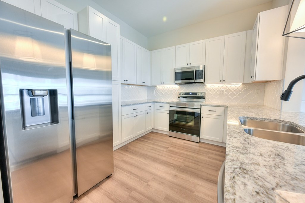 A modern kitchen with a stainless steel refrigerator and wooden flooring.
