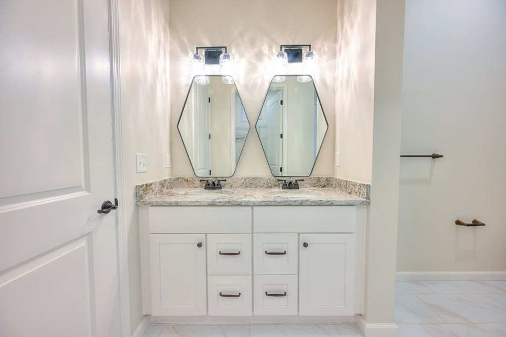 A bathroom with a marble countertop and two mirrors above it.