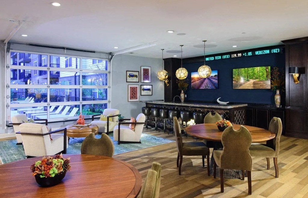 A living room with a wooden table and chairs, a sofa, and a television displaying a forest scene.