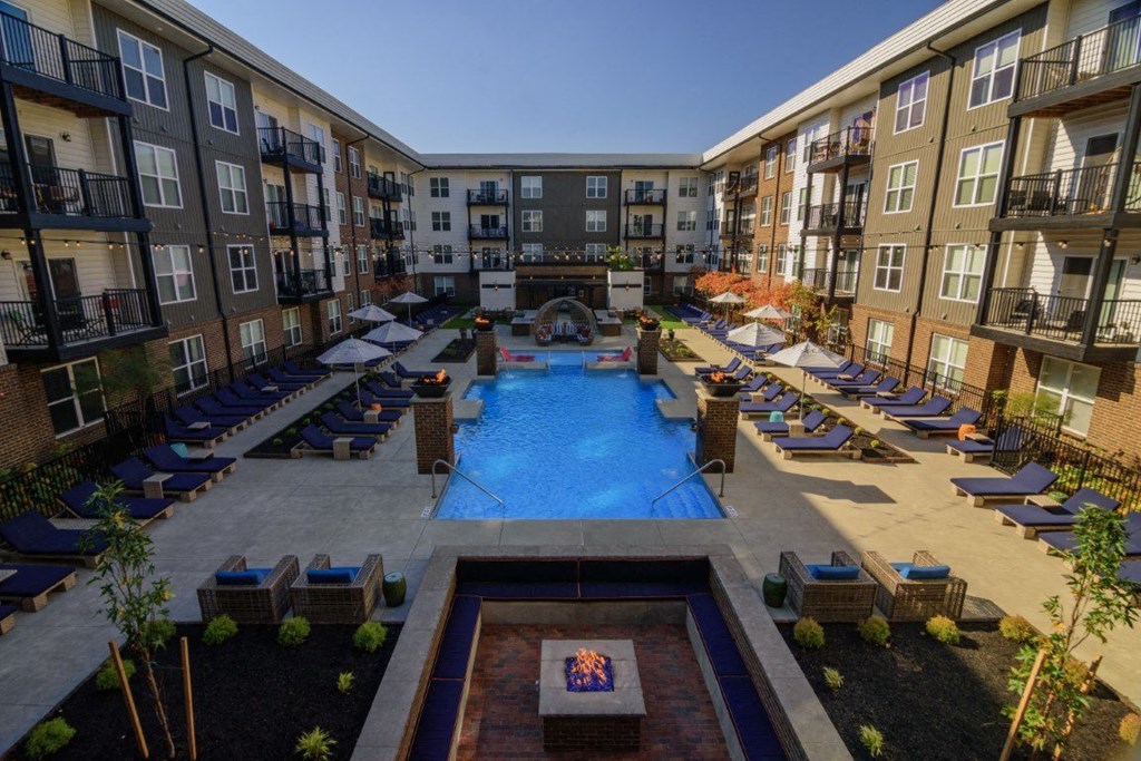 A large swimming pool surrounded by lounge chairs and umbrellas in a courtyard surrounded by apartment buildings.
