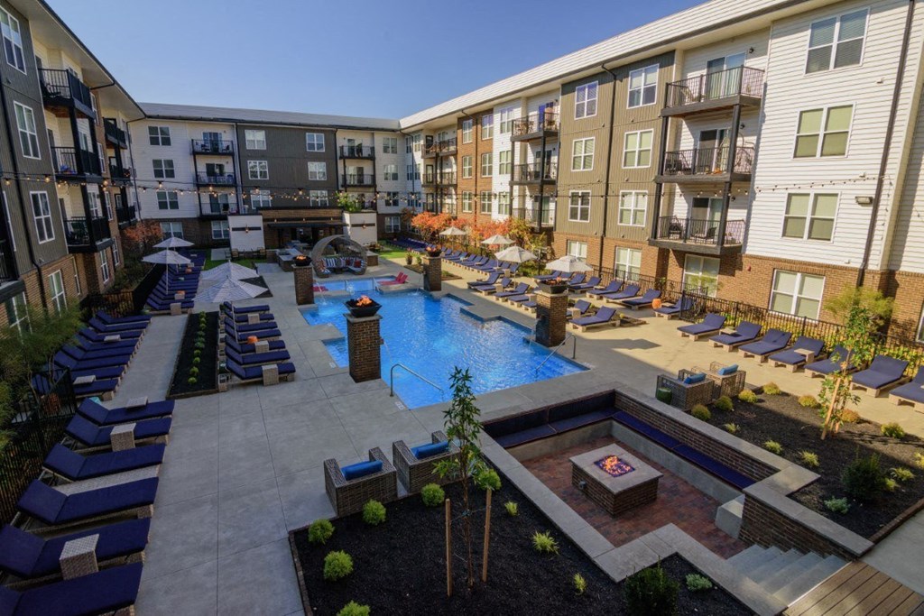 A large outdoor pool area with lounge chairs and a hot tub surrounded by apartment buildings.