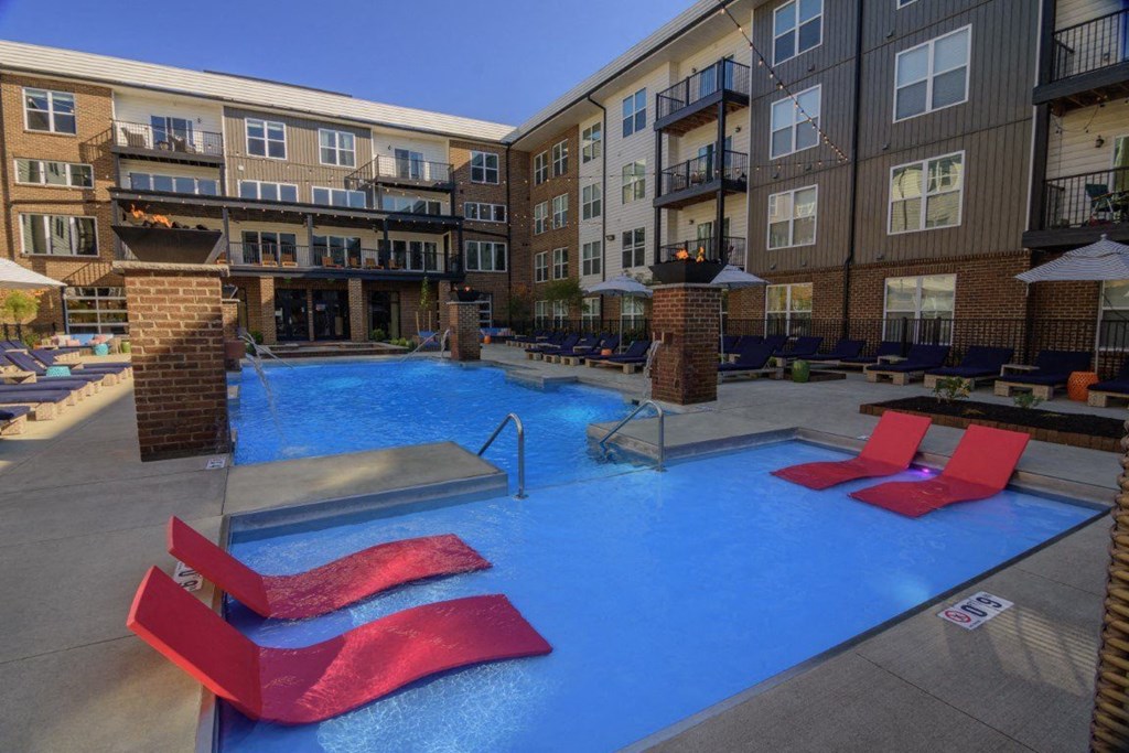 A pool with red chairs and a building in the background.