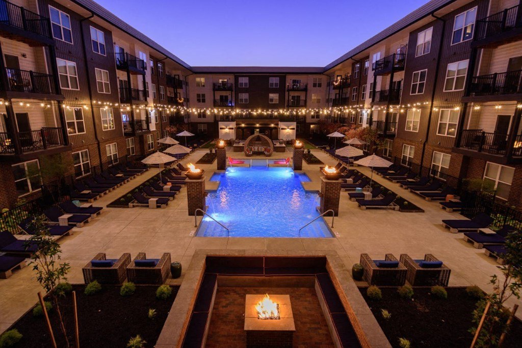 A large outdoor pool surrounded by lounge chairs and umbrellas in a courtyard.