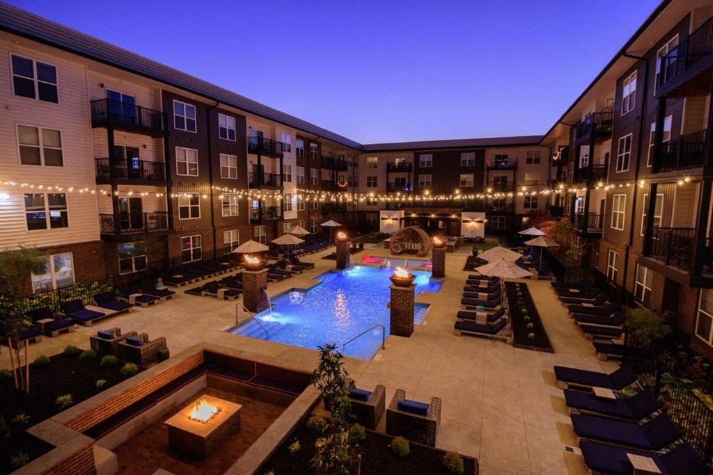 A pool surrounded by lounge chairs and lit string lights.