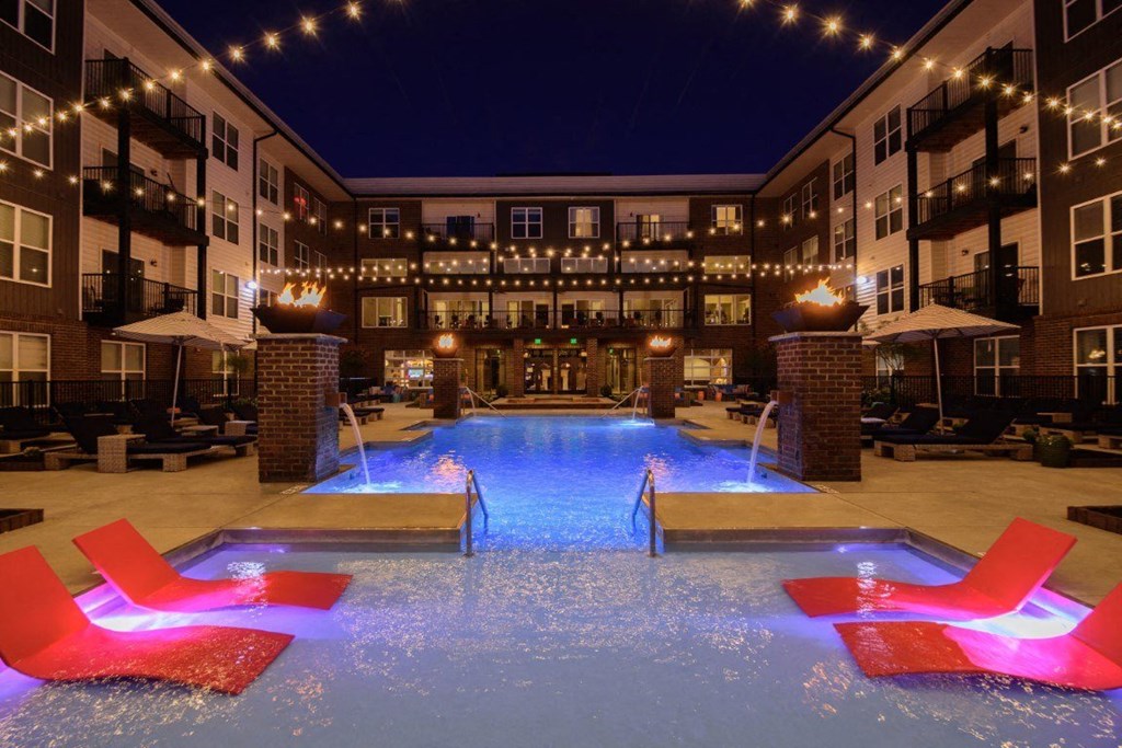 A pool with red chairs and lights around it.