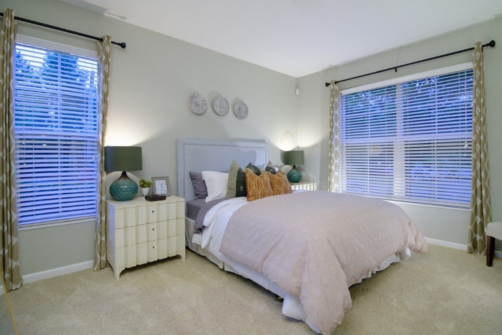 A bedroom with a bed, nightstand, and window with curtains.