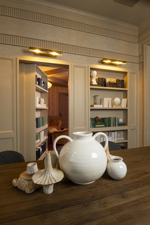 A white jug sits on a table in front of a shelf with books and other items.