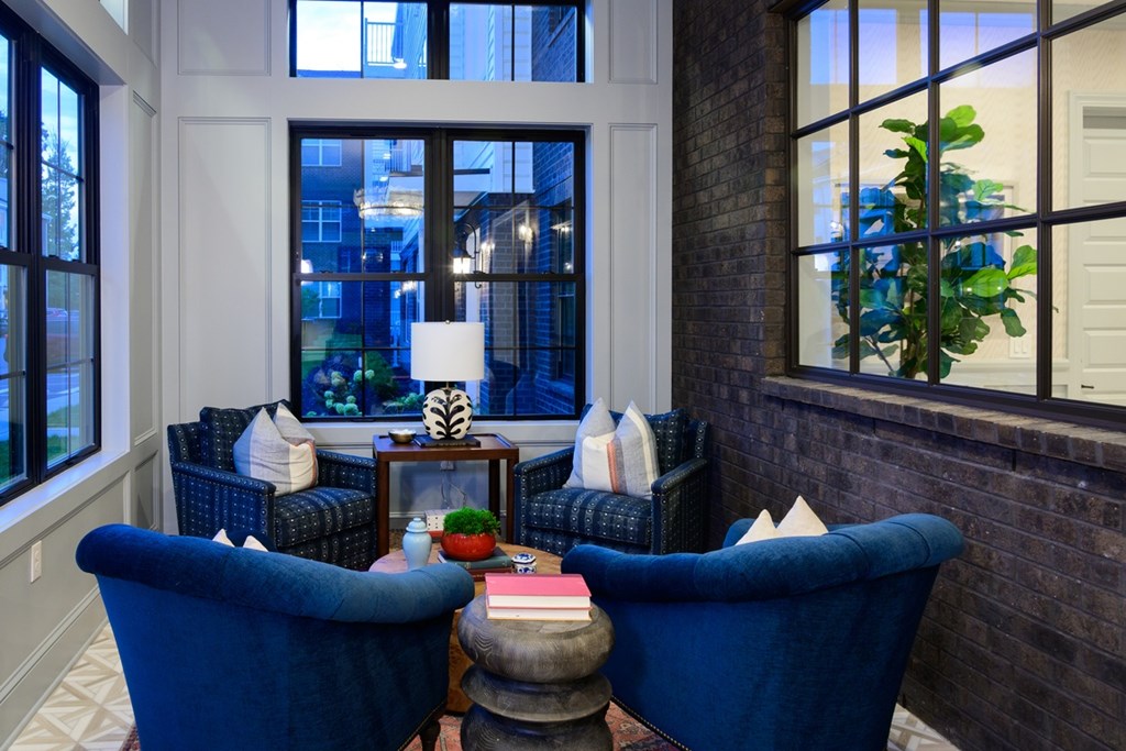 Two blue chairs are facing a table with a lamp and a vase on it.