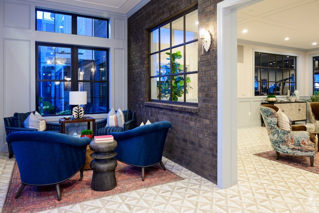 A living room with a blue chair and a table with a lamp on it.