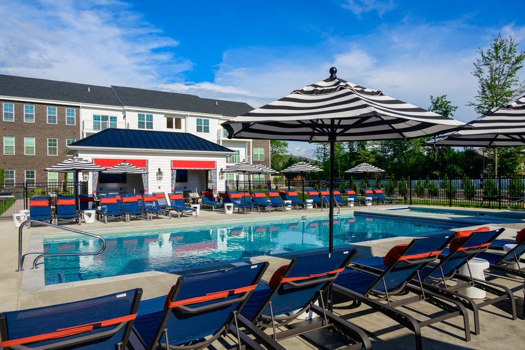 A pool area with sun loungers and umbrellas in front of a building.