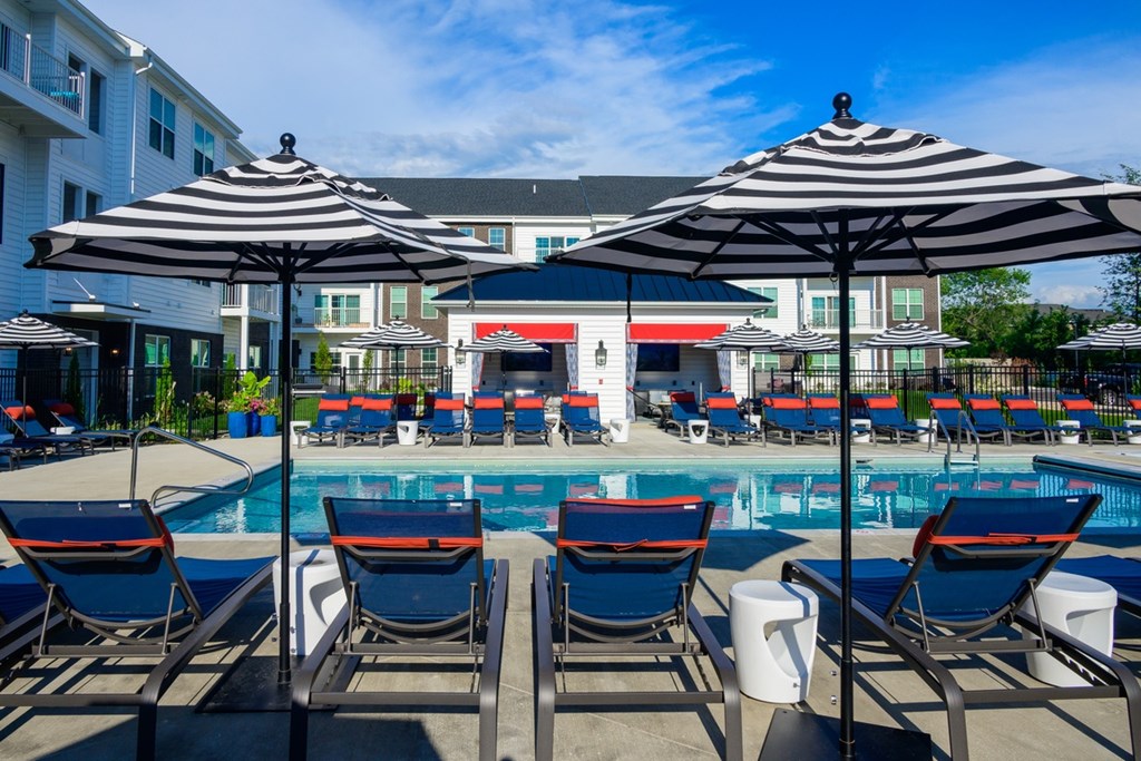 A pool area with chairs and umbrellas in front of a building.