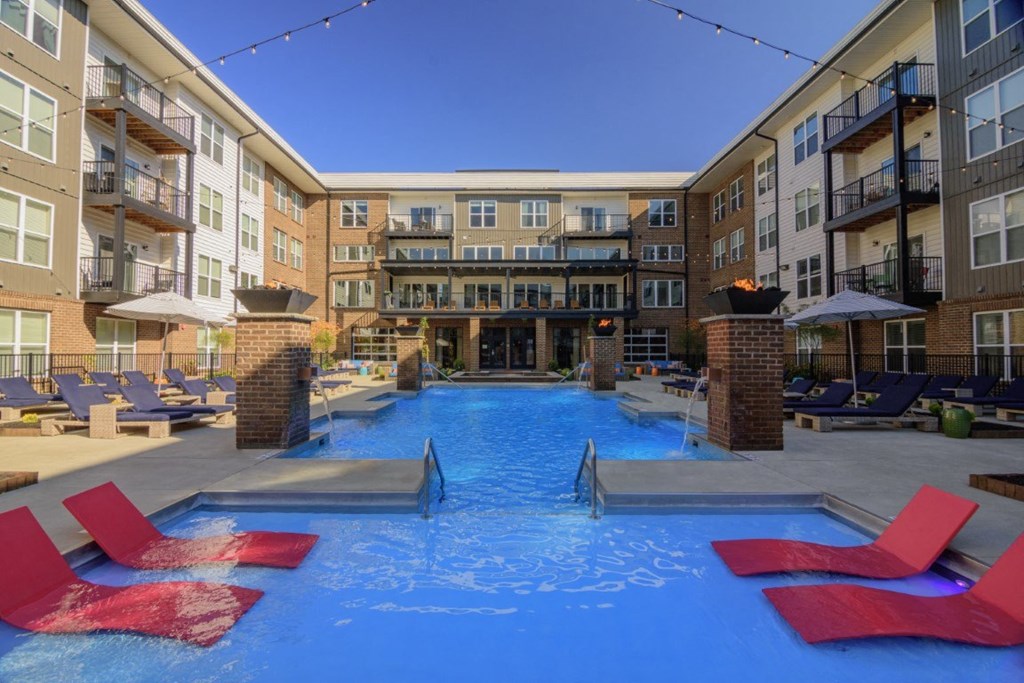 an outdoor pool with red chairs and an apartment buildingat Madison Park Apartments, Columbus