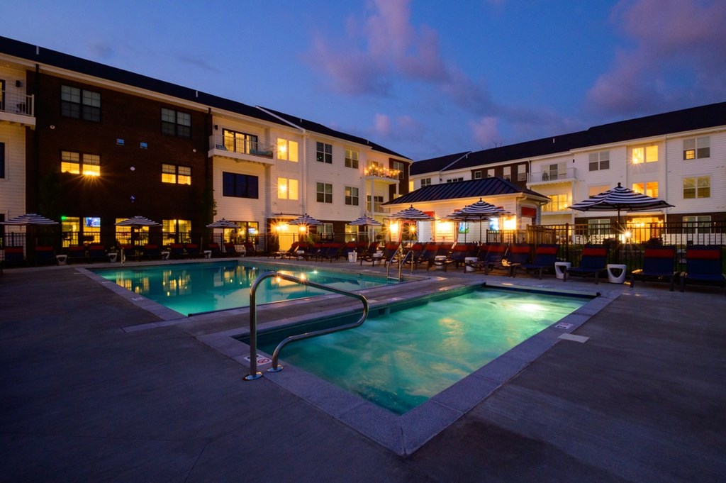A swimming pool in front of a building with lights on.
