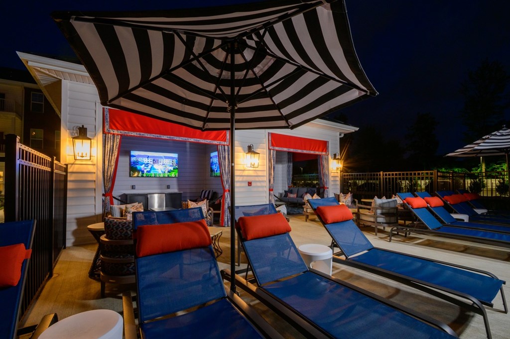 A row of lounge chairs are arranged in front of a building with a large screen and umbrella.