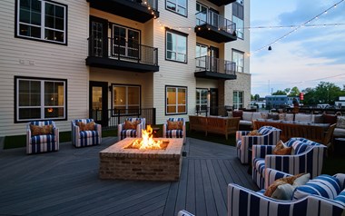 a firepit and seating area on a deck with apartment buildings in the background