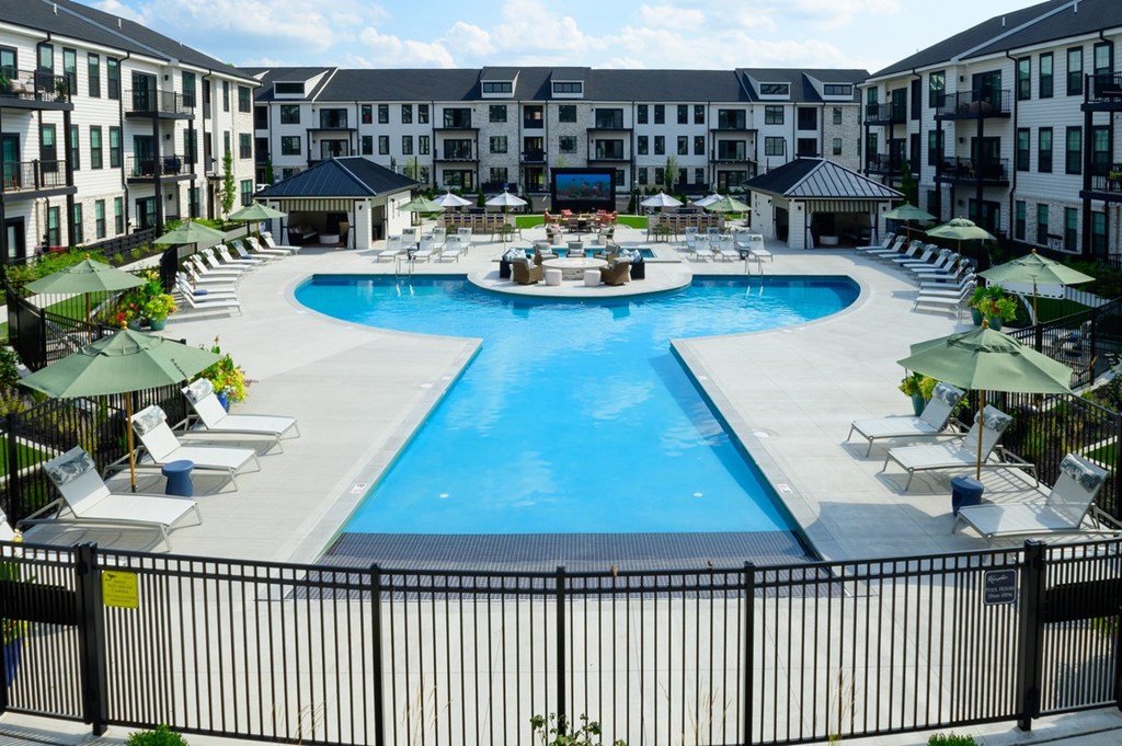 A large swimming pool surrounded by lounge chairs and umbrellas in a resort-like setting.