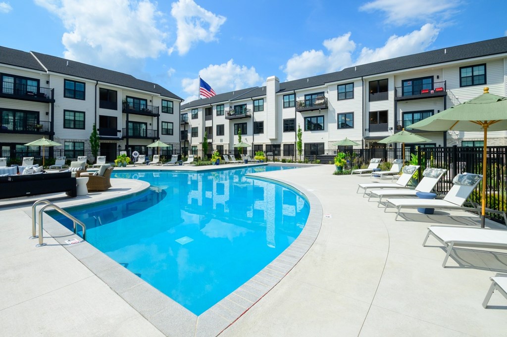 A swimming pool surrounded by lounge chairs and umbrellas in front of apartment buildings.