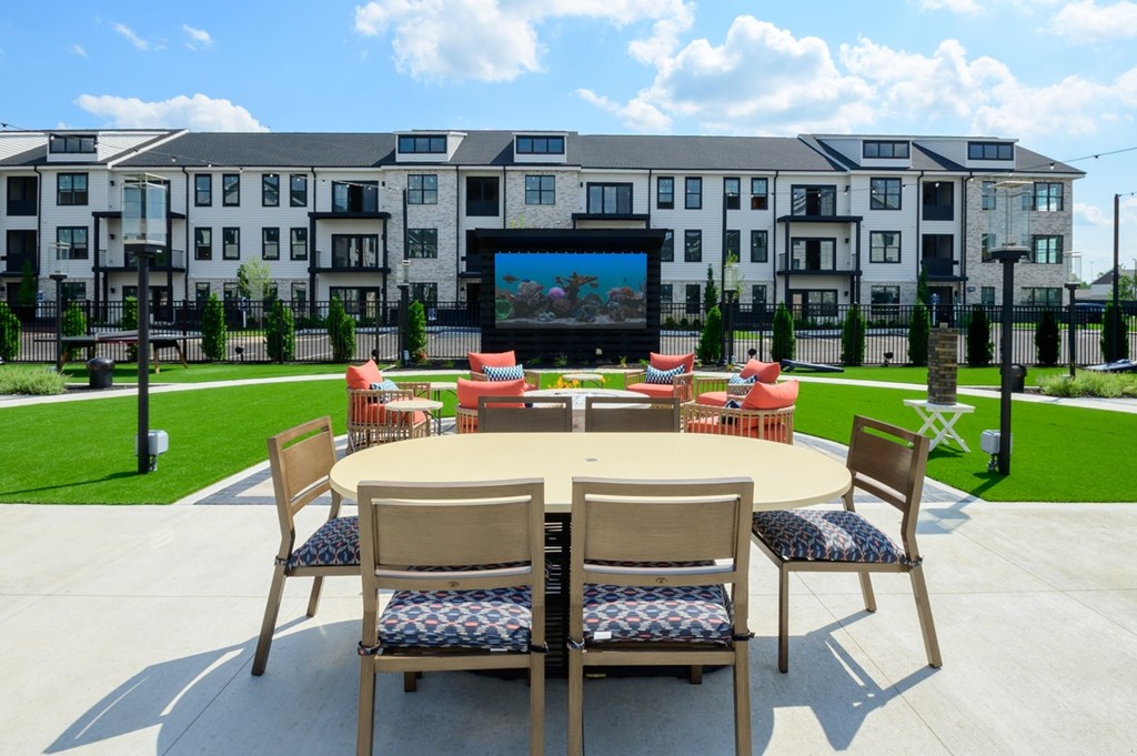 A table with chairs is set up in front of a building with a screen on it.