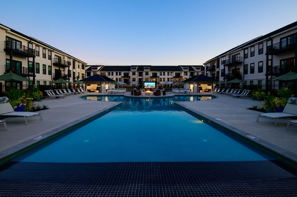 A large swimming pool in the middle of a resort surrounded by lounge chairs.