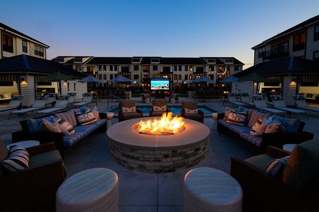 A fire pit sits in the middle of a patio surrounded by couches and tables.