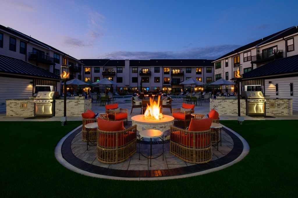 A fire pit in the middle of a grassy area surrounded by chairs.