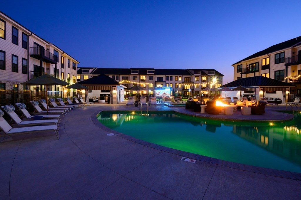 A pool area at a hotel with lounge chairs and a lit fire pit.