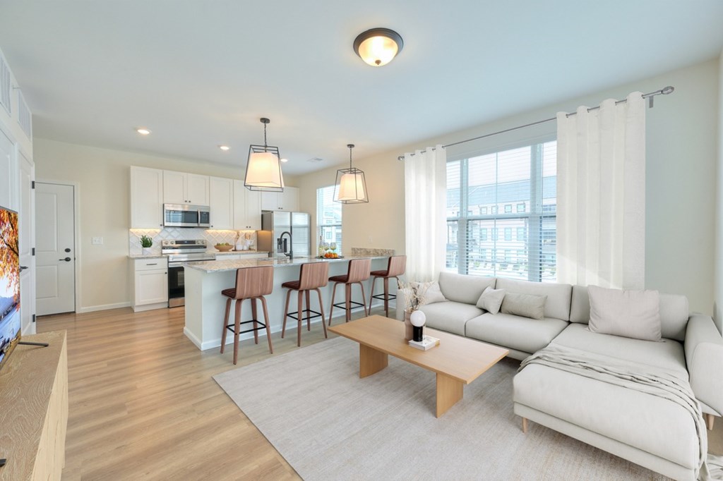 A well-lit, modern living room with a kitchen in the background.