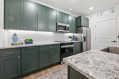 A kitchen with green cabinets and a marble countertop.