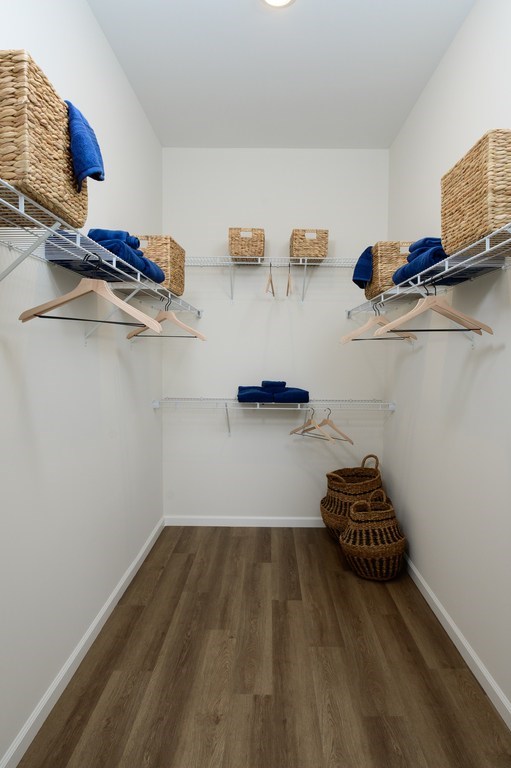 A room with a white wall and a wooden floor with clothes hanging on a rack.