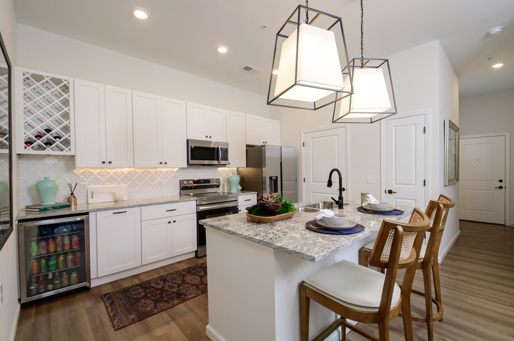 A kitchen with a white counter top and wooden chairs.