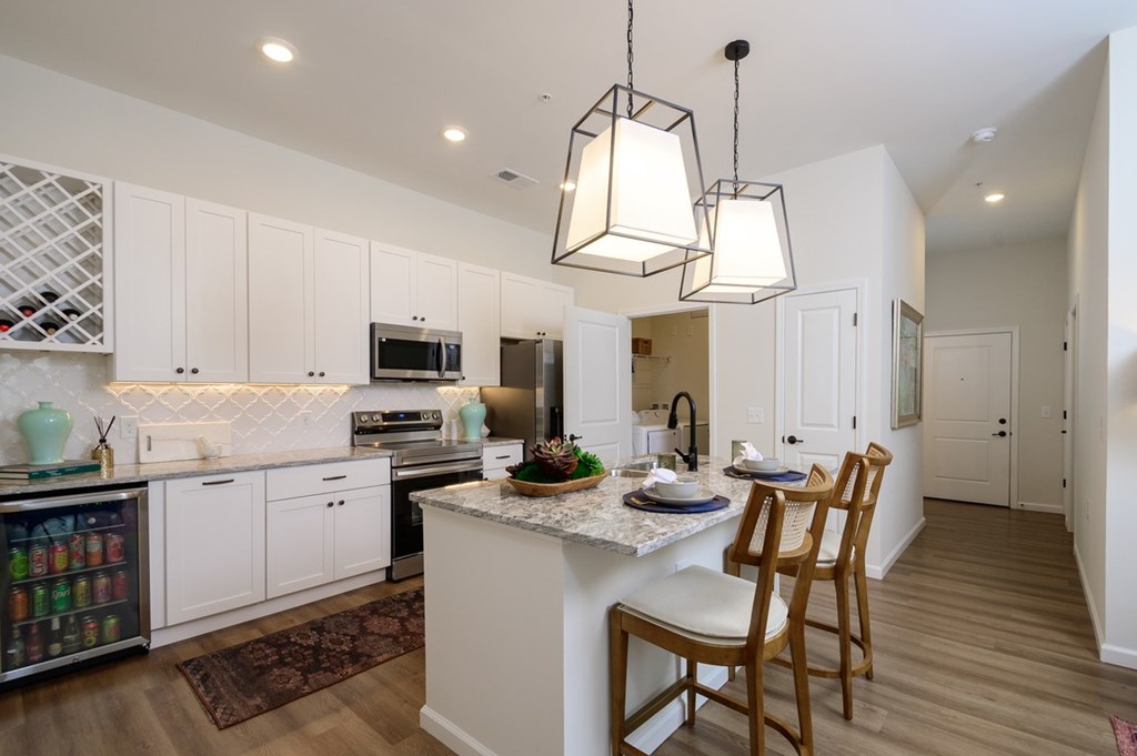 A kitchen with white cabinets and a central island with a marble top.