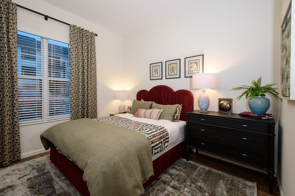 A bedroom with a bed, nightstand, and a window with curtains.